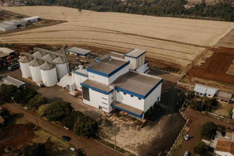 Vista aérea do Moinho Consolata com prédios de faixas azuis, silos e lavoura ao fundo